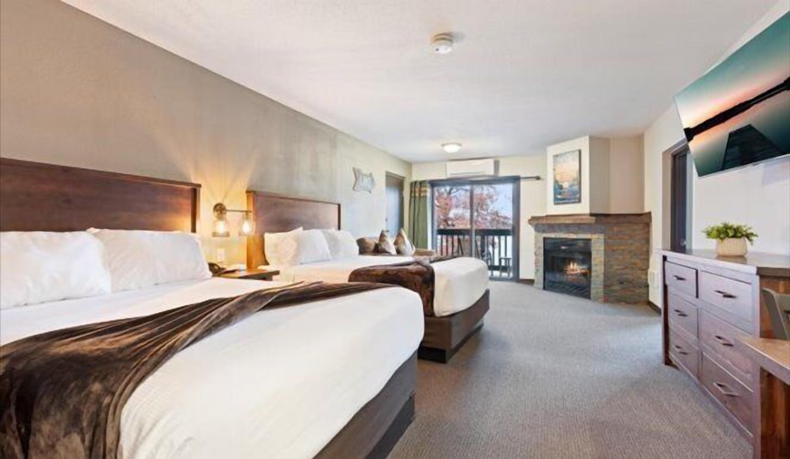 A hotel room with two beds, a fireplace, a TV, and a balcony.