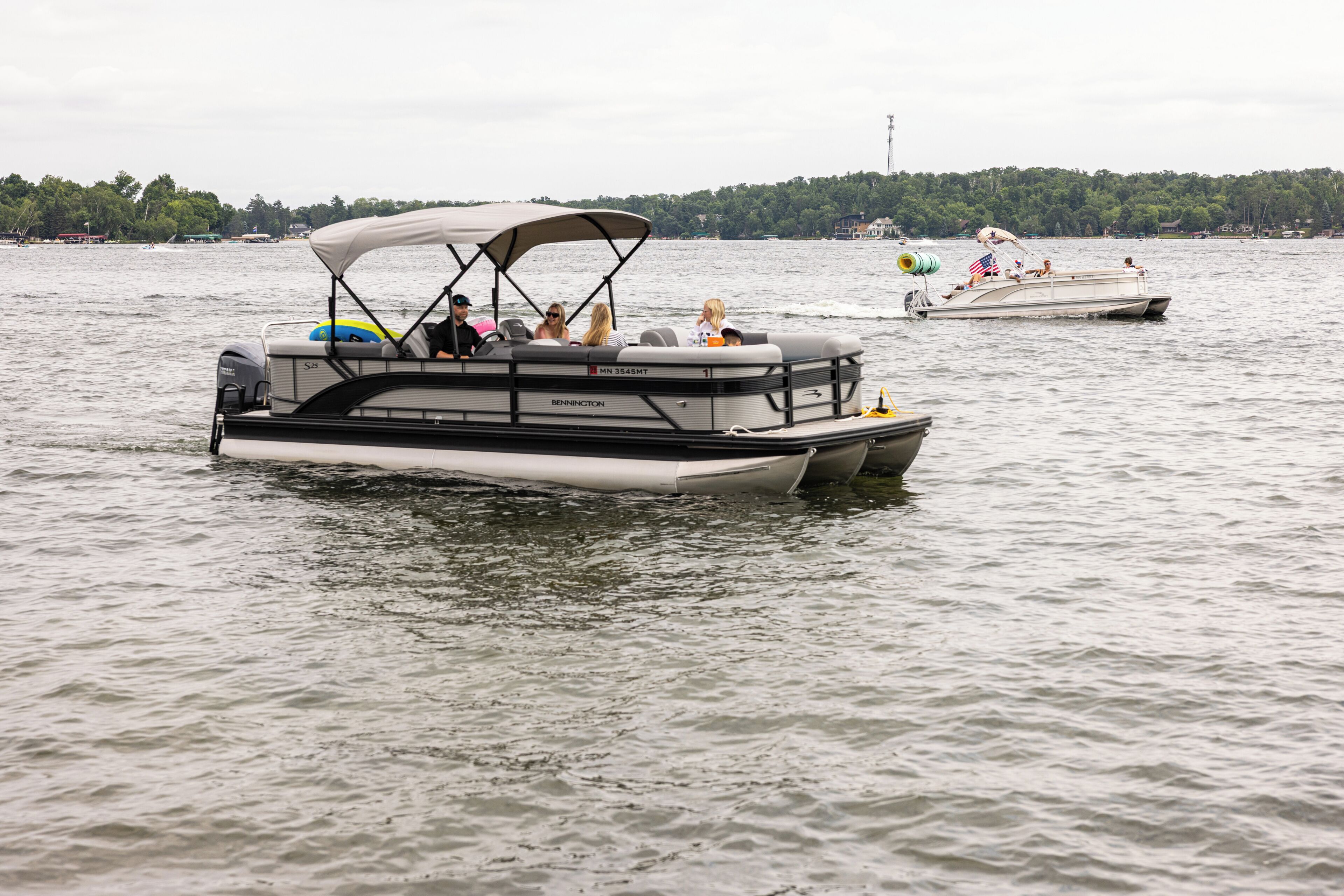 A pontoon boat with a covered seating area and a motor, floating on a lake.