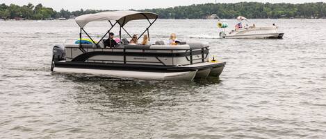 A pontoon boat with a covered seating area and a motor, floating on a lake.