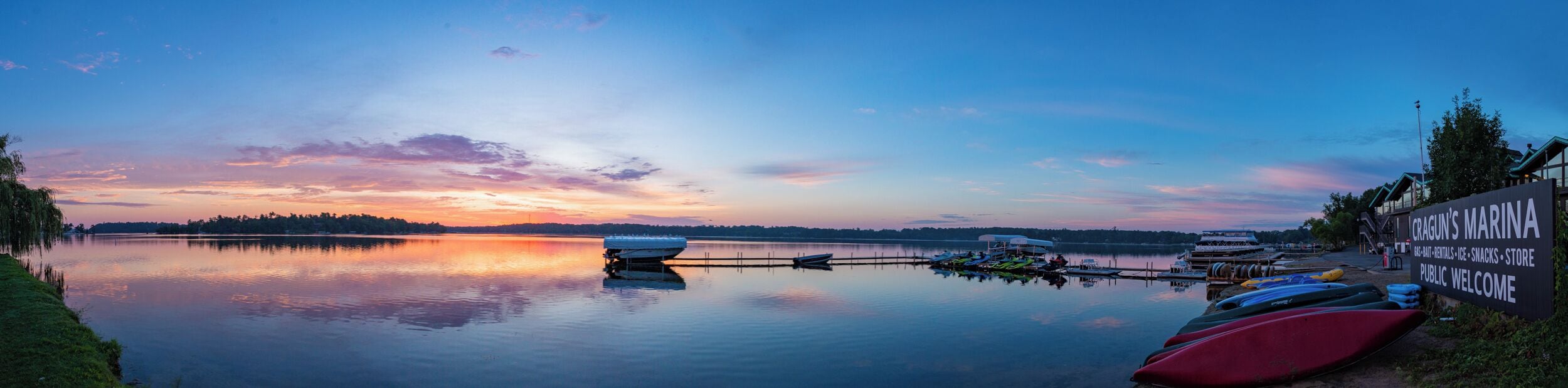 A marina with boats docked, a calm lake, and a sunset sky.