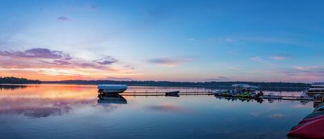 A marina with boats docked, a calm lake, and a sunset sky.