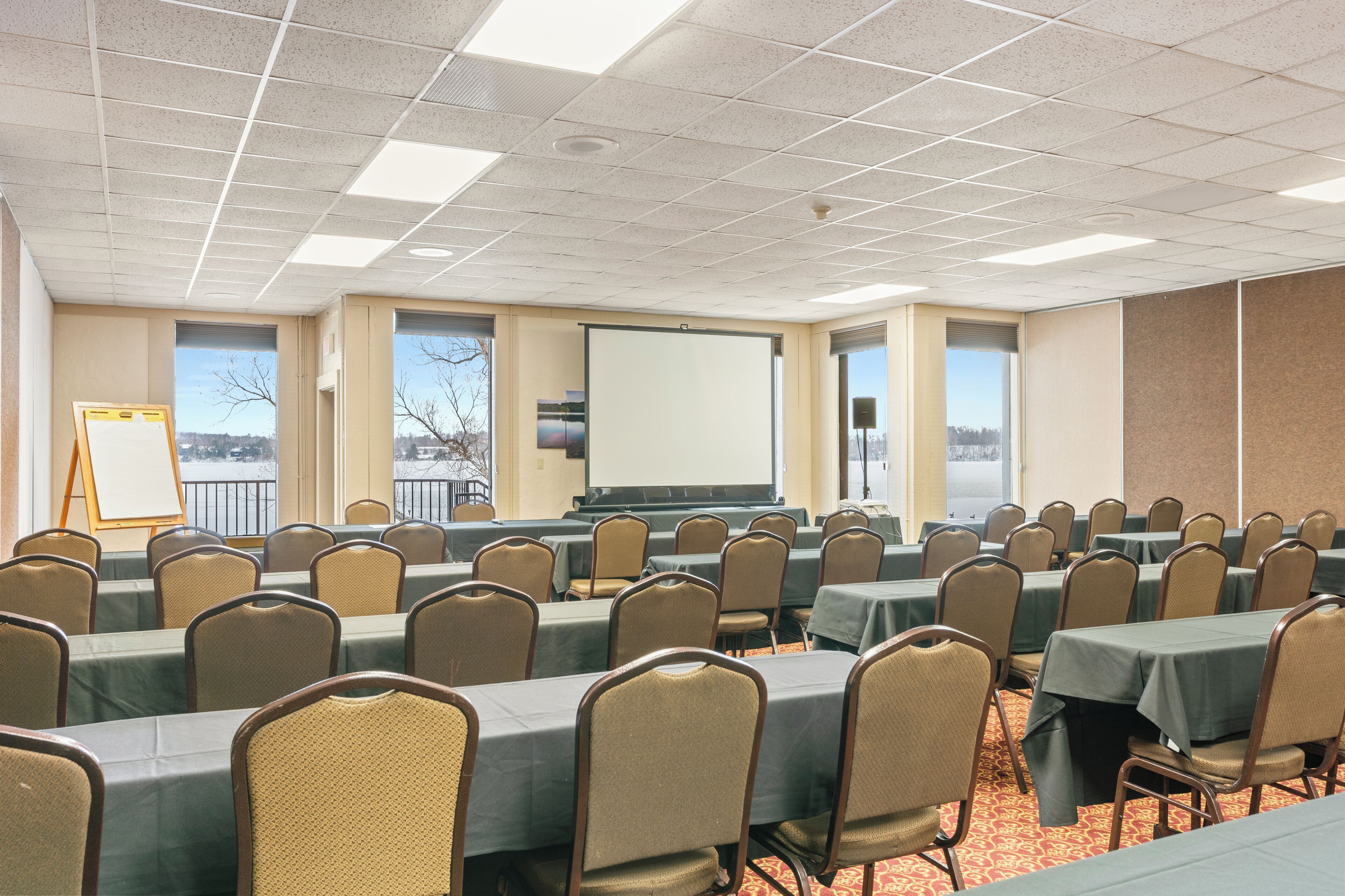 A conference room with multiple tables and chairs, a whiteboard, and a projection screen.