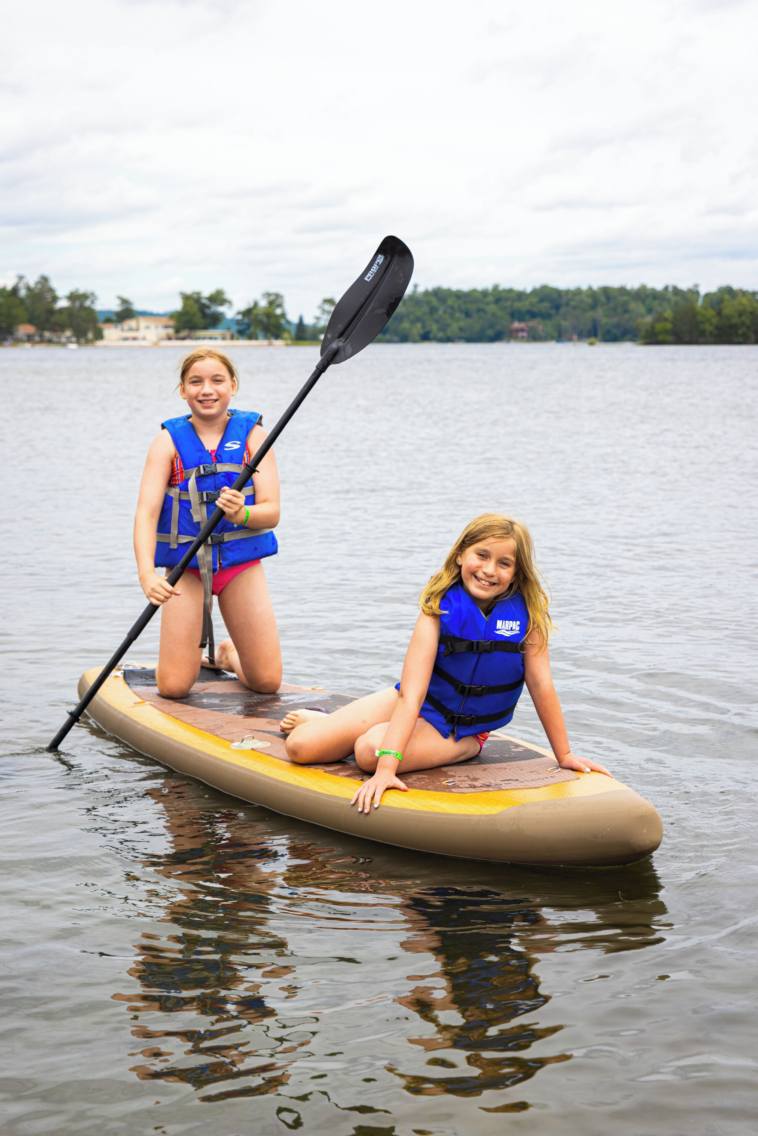 Two individuals on a paddleboard in a body of water with a distant shoreline.