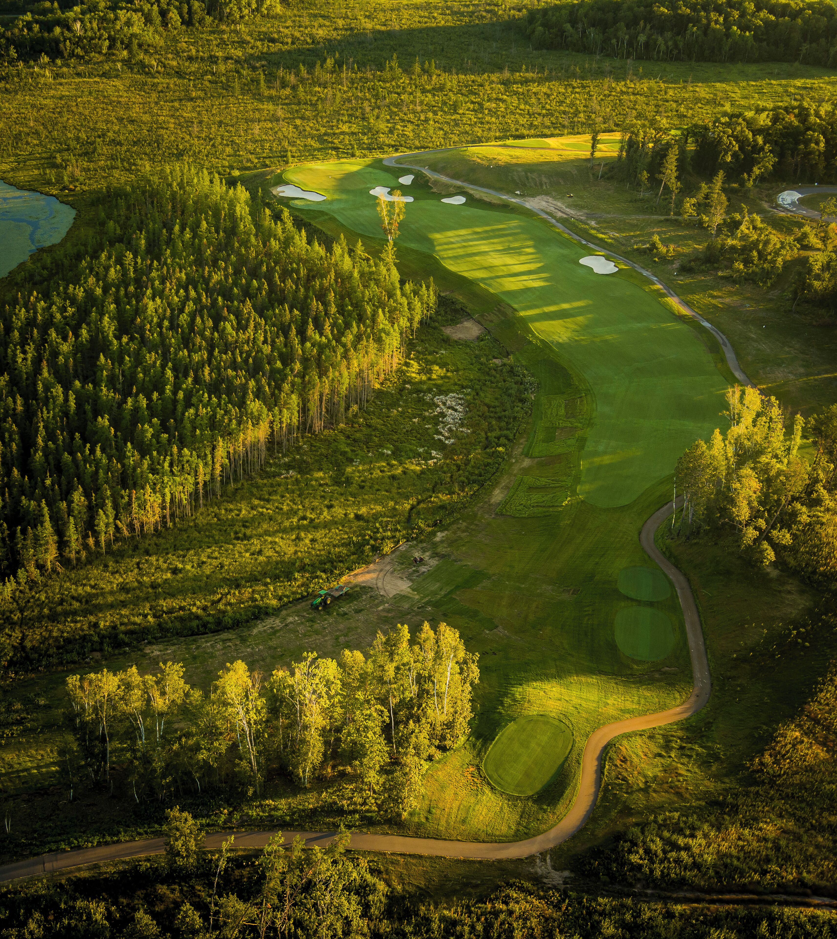 An aerial view of a golf course with a winding road, dense forest, and several water hazards.
