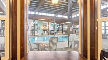 A poolside area with a wooden table and chairs, a pool, and a view of the interior with multiple levels and seating areas.