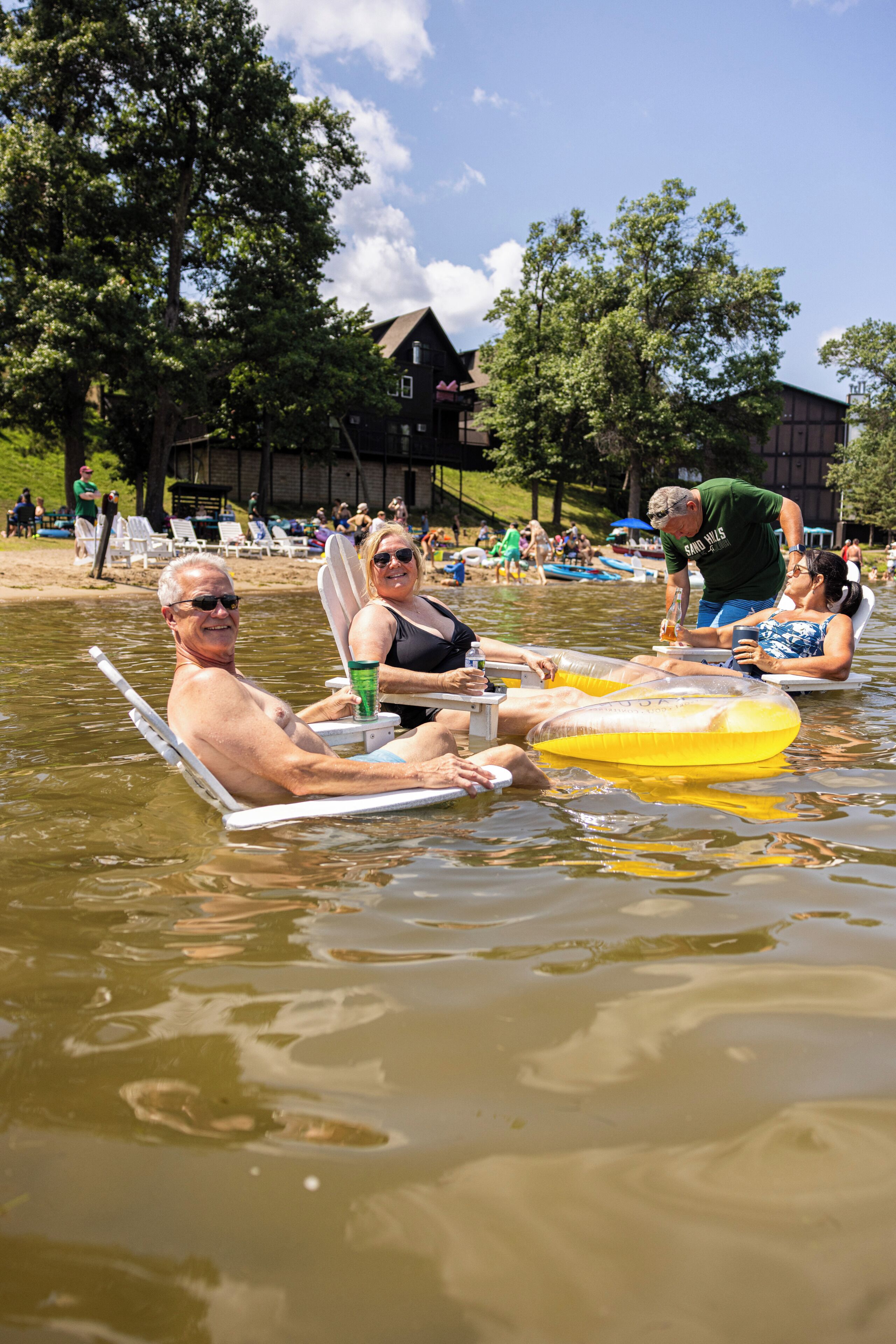 Eine Gruppe von Menschen treibt auf dem Wasser, manche auf Luftmatratzen. Im Hintergrund sind ein Gebäude und Bäume zu sehen.
