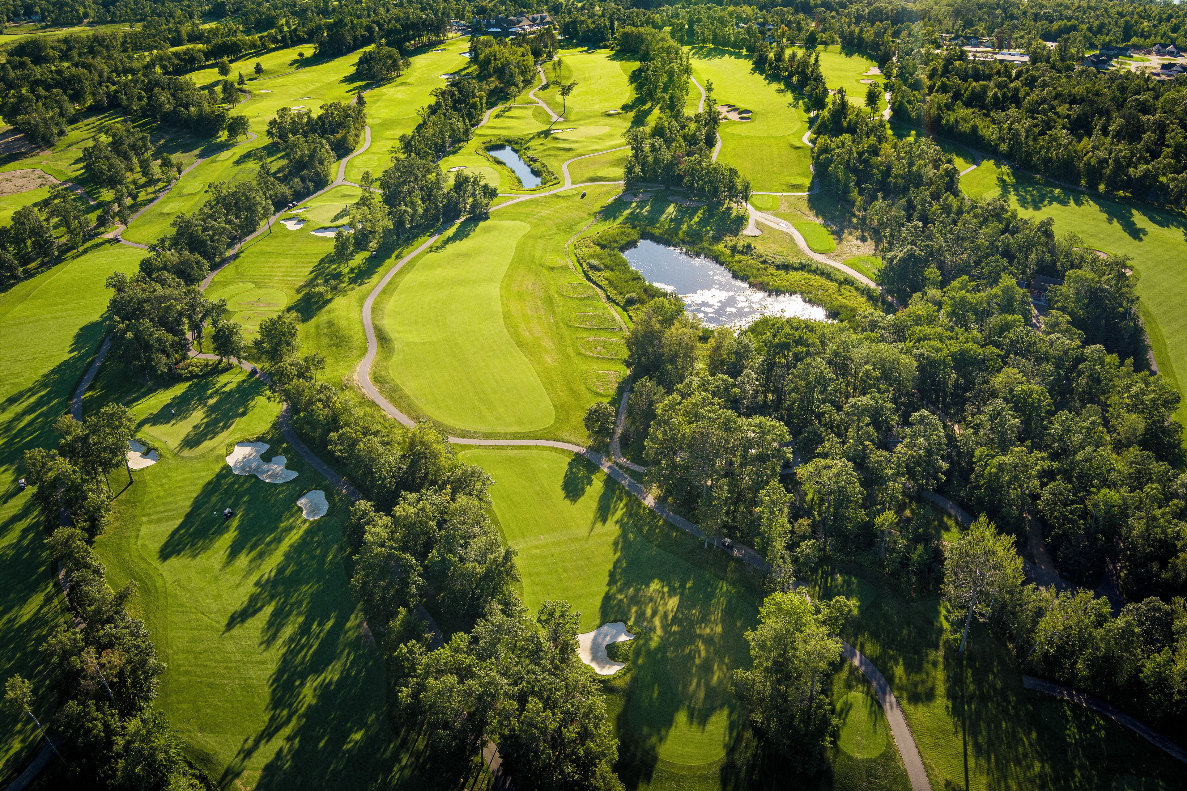 An aerial view of a golf course with multiple holes, water hazards, and surrounding wooded areas.