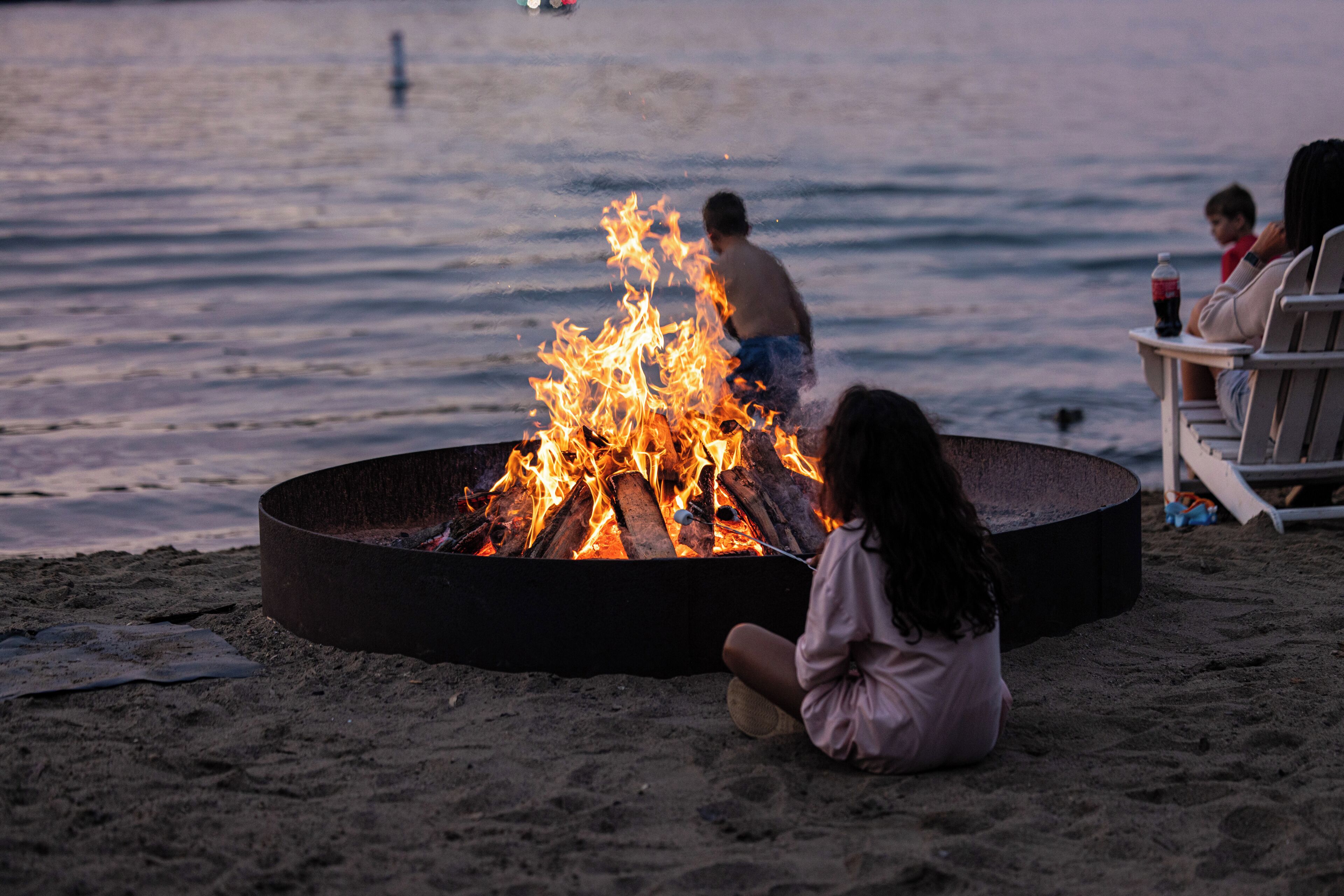 A beach scene with a campfire, a person sitting, and a person standing by the water.