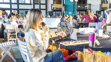 Une personne assise à une table, devant un microphone et un jeu de société, entourée d’autres tables et de chaises.