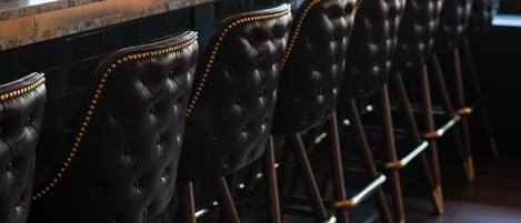 A bar area with a long counter and multiple black leather barstools with gold accents.