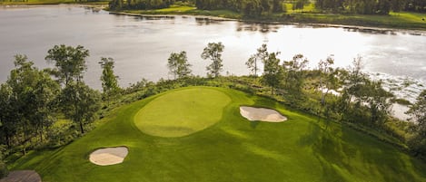 A golf course with two sand bunkers, a water body, and a forested area.