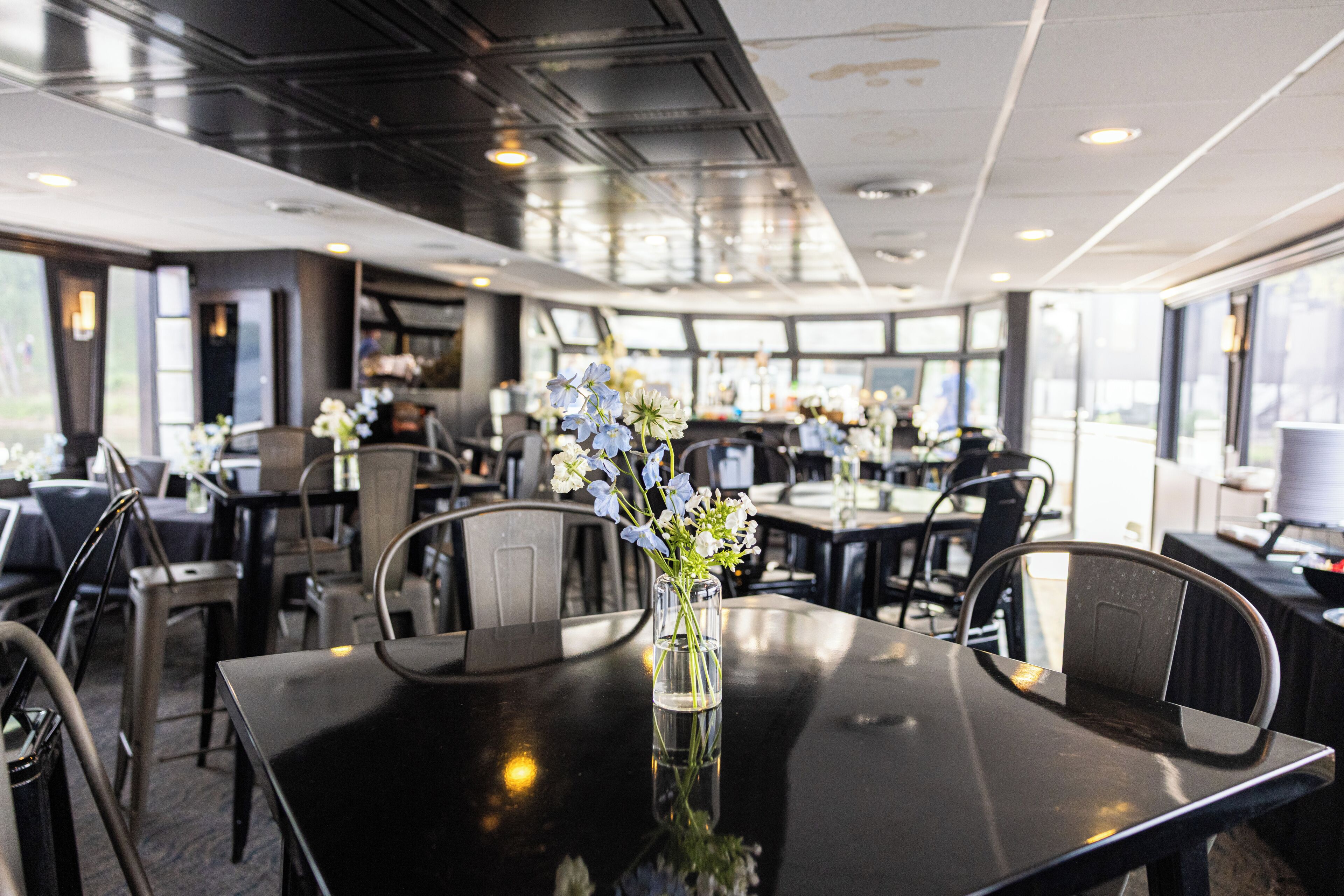 Un espace repas moderne avec des tables, des chaises et un vase rempli de fleurs.
