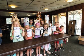 A group of children holding birth certificates in a room with a wooden table and chairs. - Cragun's Resort & Hotel (Brainerd)