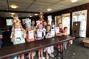 A group of children holding birth certificates in a room with a wooden table and chairs.