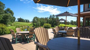 An outdoor patio area with Adirondack chairs and tables, a golf course in the background, and a clear blue sky.