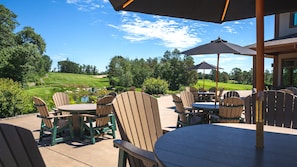 An outdoor patio area with Adirondack chairs and tables, a golf course in the background, and a clear blue sky.