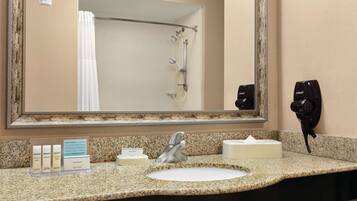 A hotel bathroom with a granite countertop, a sink, a mirror, a shower, and a hairdryer.