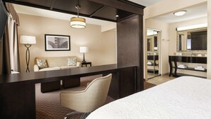 A hotel room with a bed, a desk, a chair, a lamp, a framed picture on the wall, and a mirror. - Hampton Inn & Suites Enid (Enid)