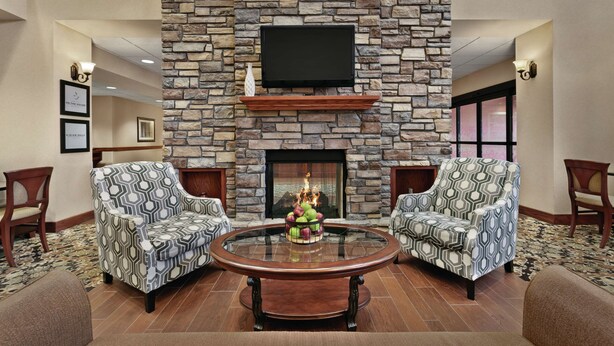 A lobby with a stone fireplace, two patterned armchairs, a round glass coffee table, and a flat-screen TV mounted on the wall. - Hampton Inn & Suites Enid (Enid)