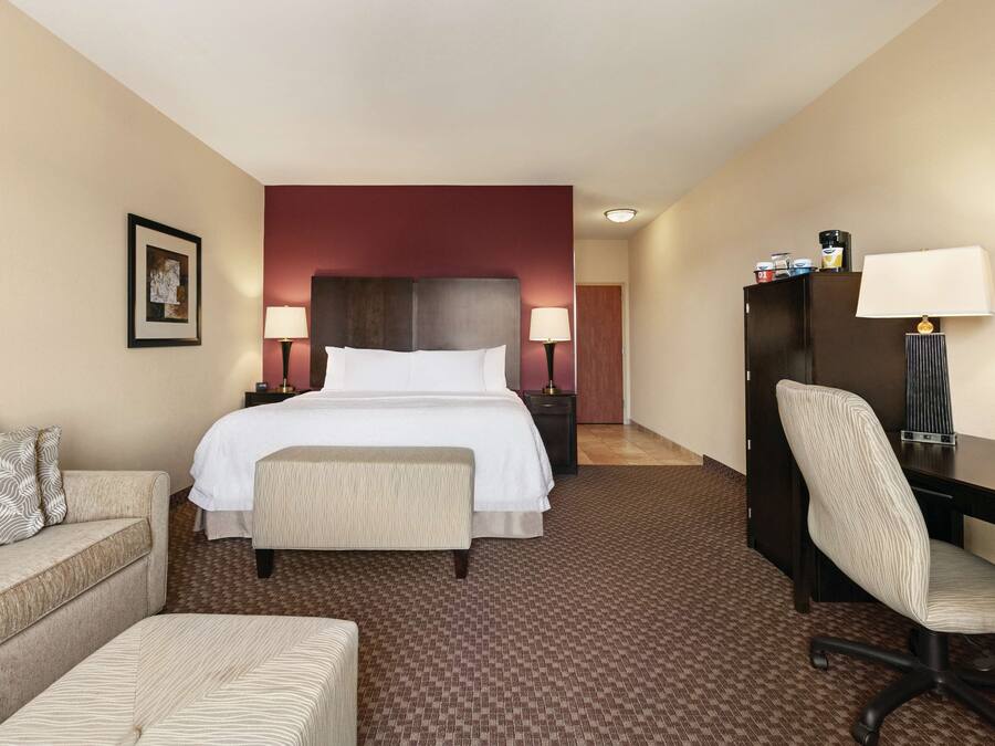 A hotel room with a large bed, a desk, a chair, a sofa, and two bedside tables with lamps.