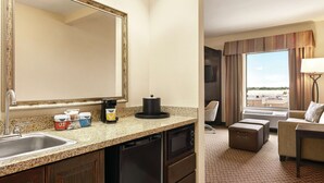 A hotel room with a kitchenette, a large mirror, a sofa, a window with a view, and a lamp. - Hampton Inn & Suites Enid (Enid)