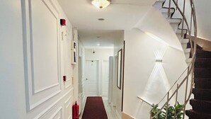A hallway with a brown tiled floor, white walls, a red fire extinguisher, and a spiral staircase with a white railing. - Anadolu Hotel (Istanbul)