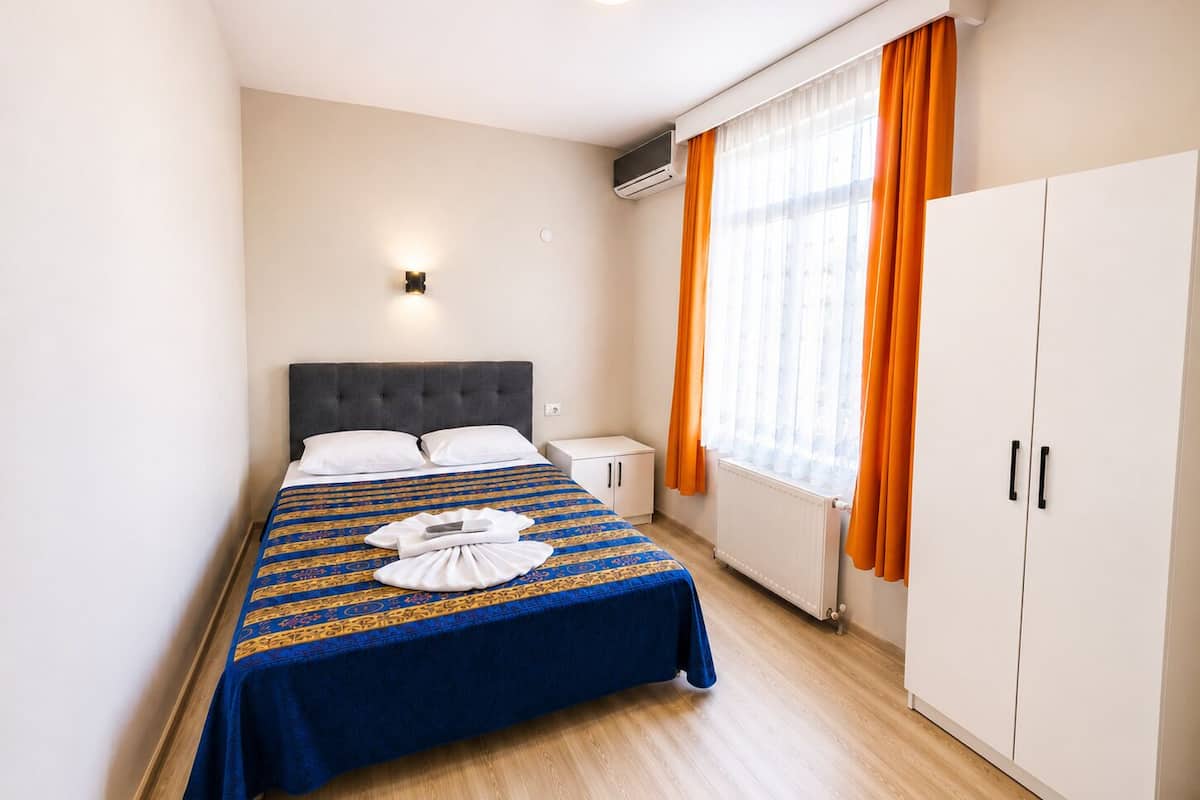 A hotel room with a bed, a nightstand, a wardrobe, and a window with curtains.