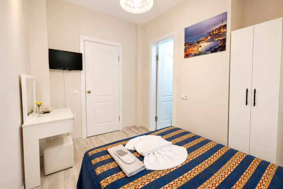 A hotel room with a bed, a desk, a television, and a wardrobe.