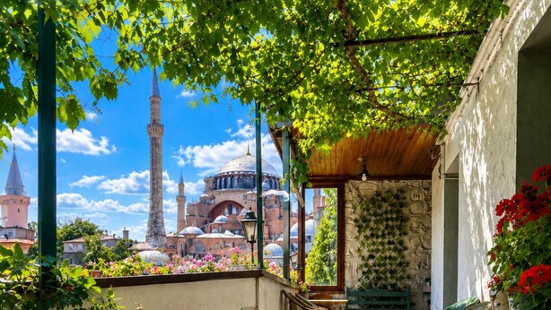 An outdoor patio with a view of a historic building, wicker furniture, and potted plants. - Anadolu Hotel (Istanbul)
