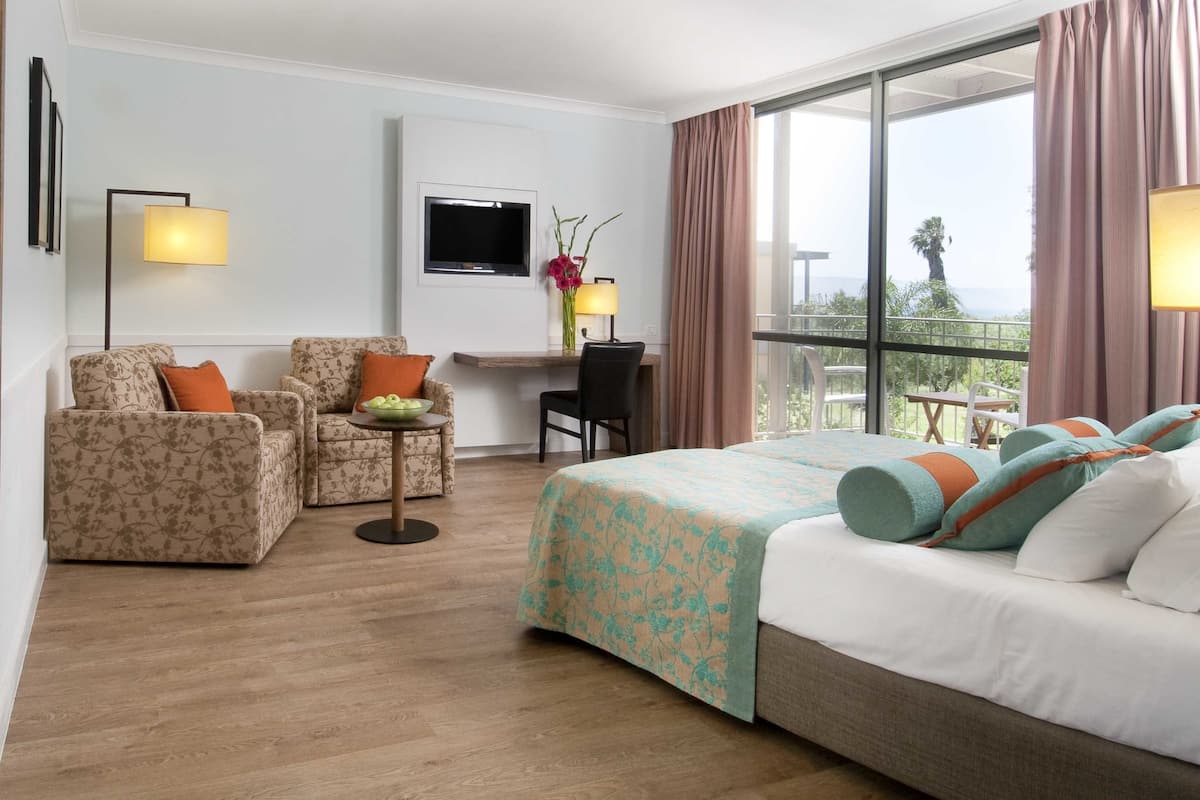 Ein Hotelzimmer mit einem Bett, zwei Sesseln, einem Schreibtisch und einem Fernseher.