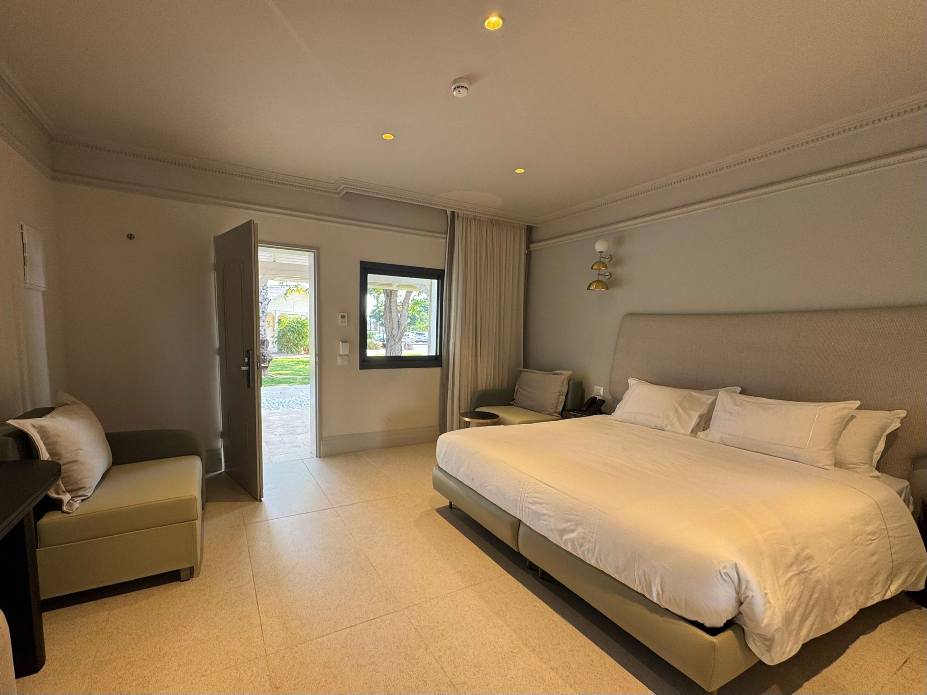 Quarto de hotel com cama, escrivaninha, cadeira, janela e porta.
