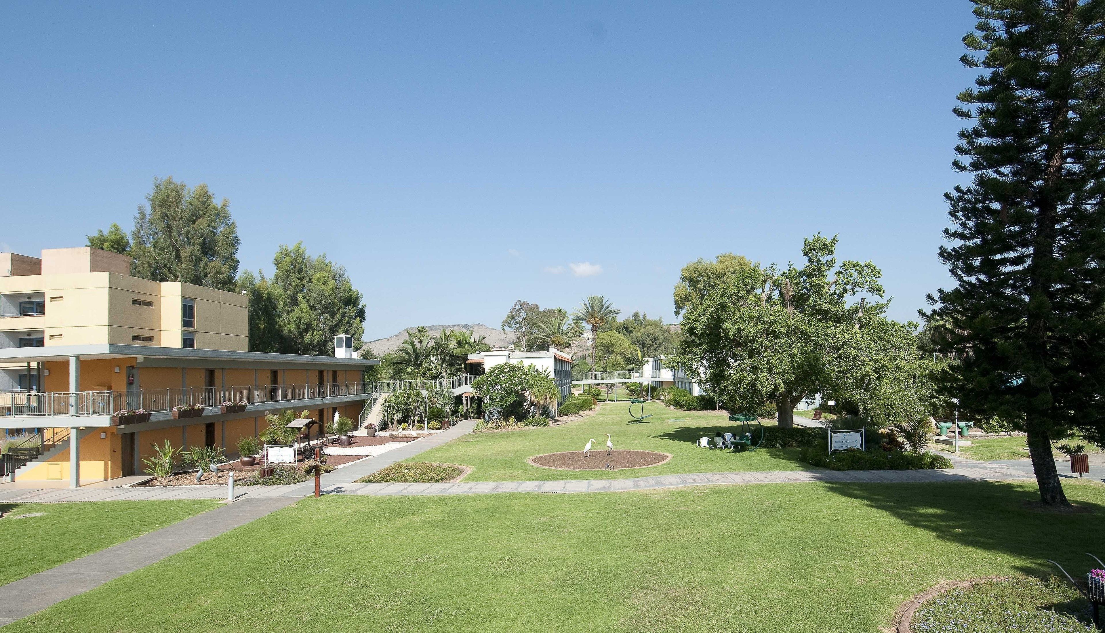 A courtyard with a lawn, a small pond, and a building with a balcony.