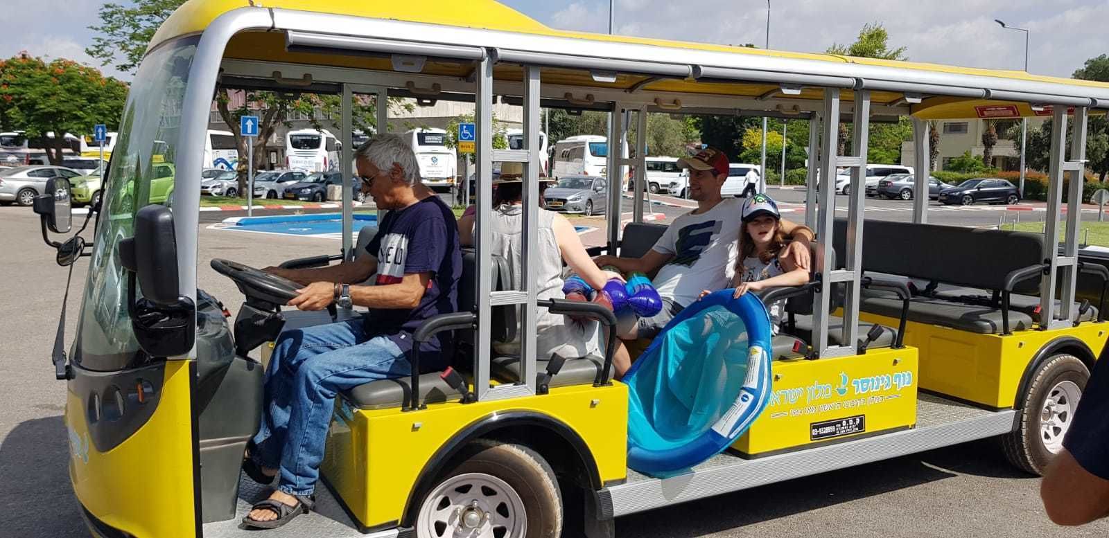 A yellow bus with passengers, including a child with a blue balloon, parked in a parking lot.