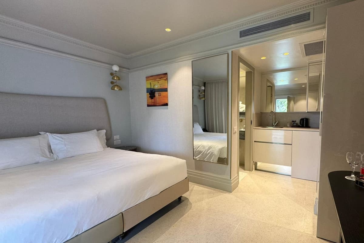 Ein Hotelzimmer mit Bett, Spiegel, Gemälde, einer Küchenzeile und einem kleinen Tisch mit Gläsern.