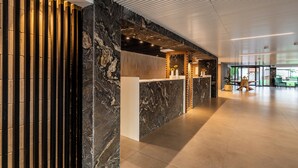 Un mostrador de recepción con una pared de mármol, un diseño de listones de madera a la izquierda y un techo moderno con iluminación empotrada.