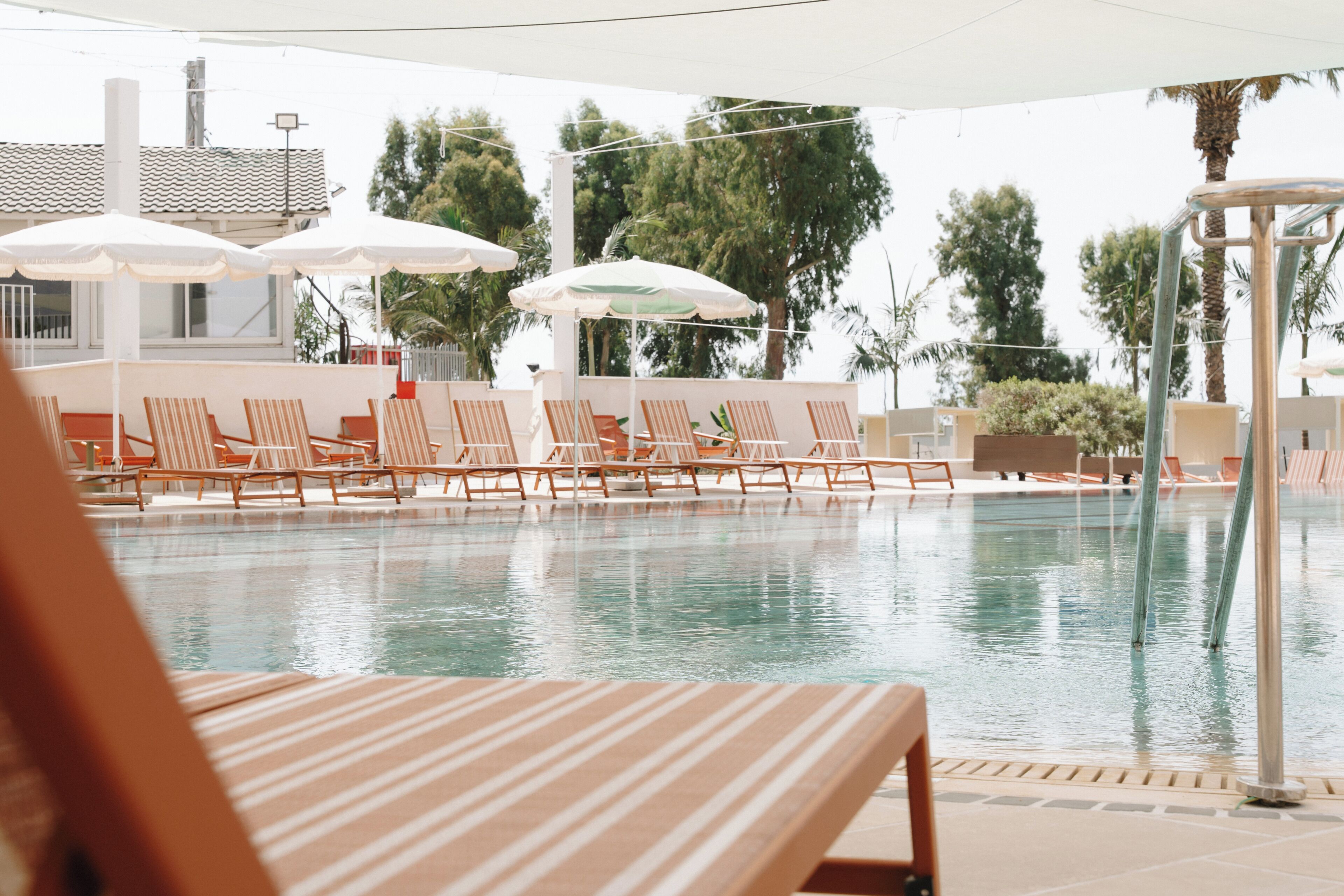 Zona de piscina con sillones de descanso y sombrillas.
