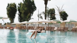 Una piscina con sillones de descanso y sombrillas, rodeada de palmeras.