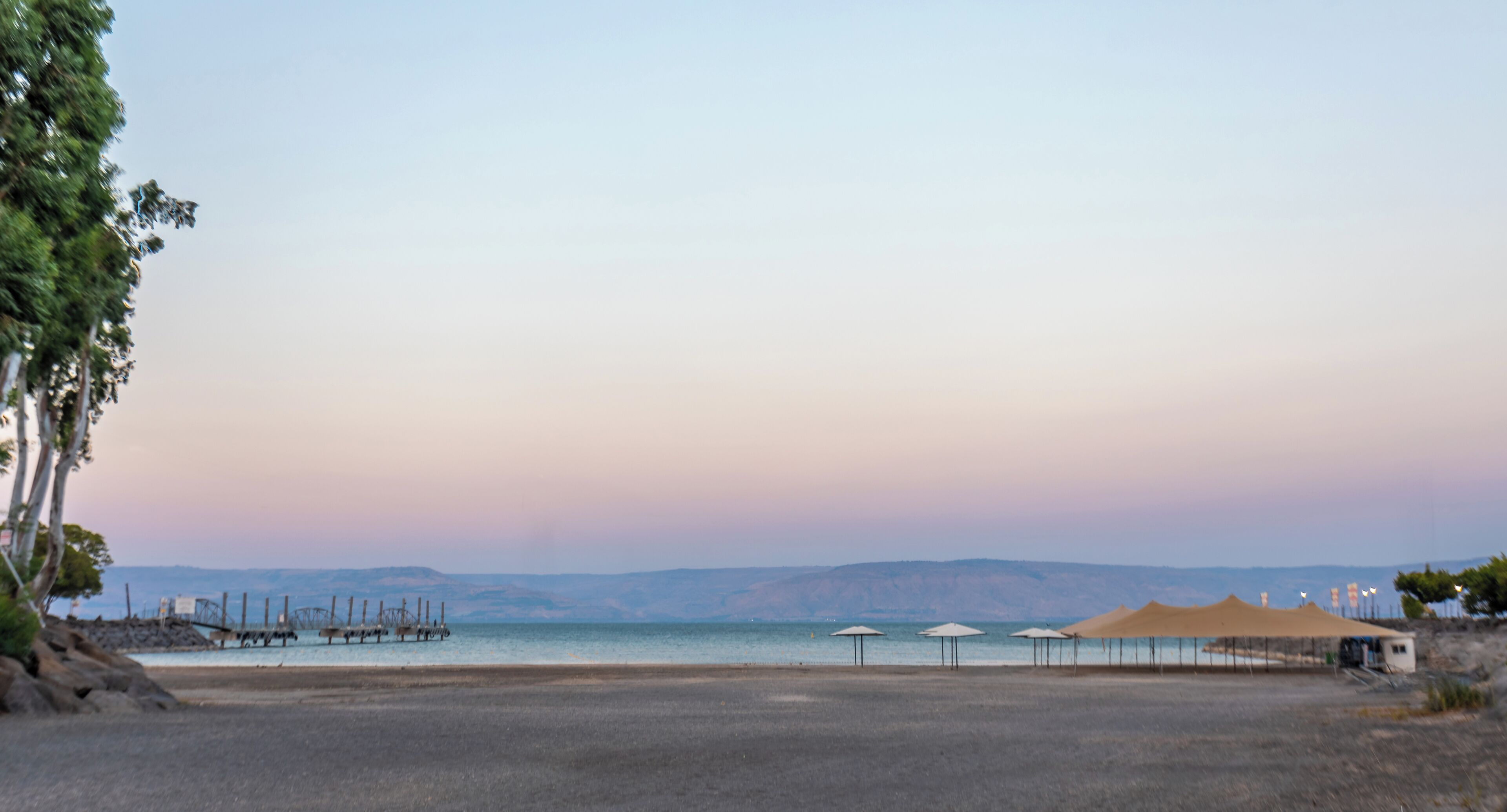 A beach with a clear sky, a few umbrellas, and a distant mountain range.