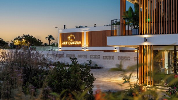 Un hotel moderno con un cartel llamativo que dice "Nof Ginosar". Presenta un diseño contemporáneo con techo plano y ventanas amplias.