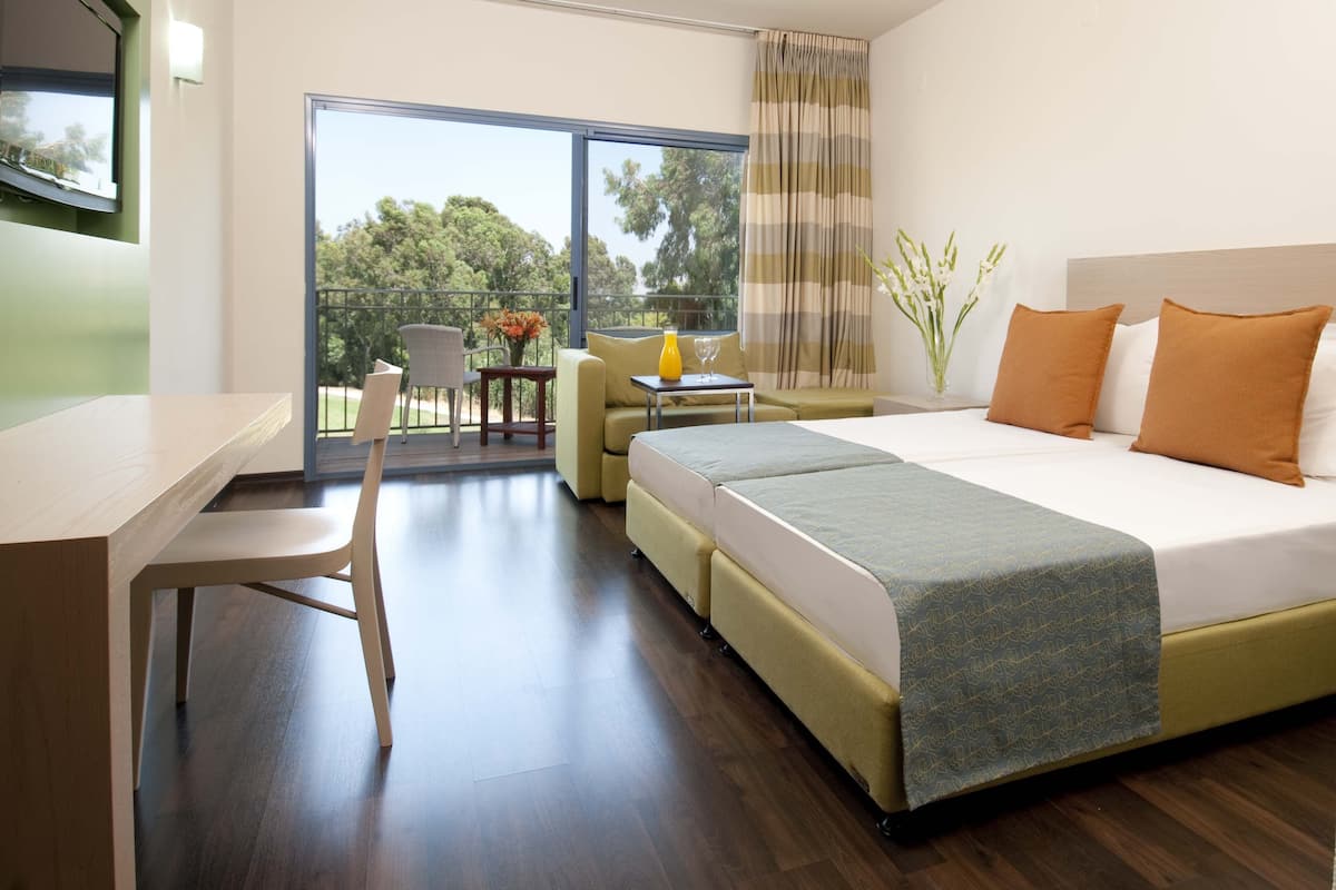 Ein modernes Hotelzimmer mit einem großen Bett, einem Schreibtisch und einem Balkon mit Blick auf Bäume.
