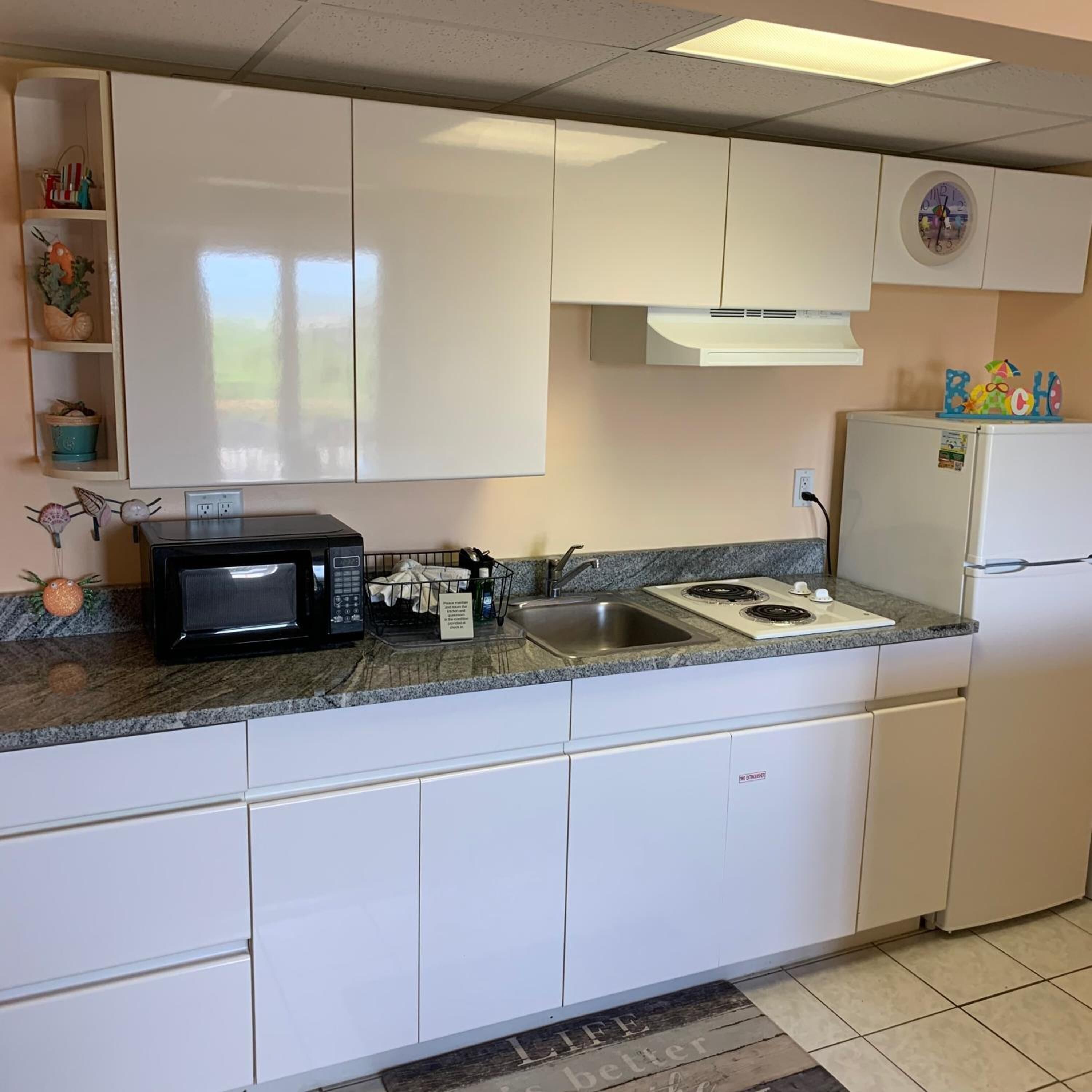 Een keuken met witte kasten, een zwarte magnetron, een fornuis en een koelkast.