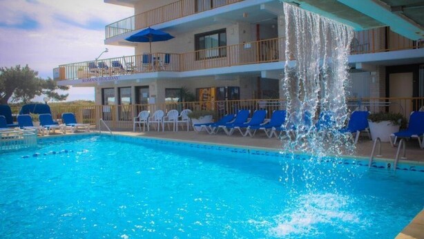 A swimming pool with blue chairs and a water feature. - Roman Holiday Motel (North Wildwood)