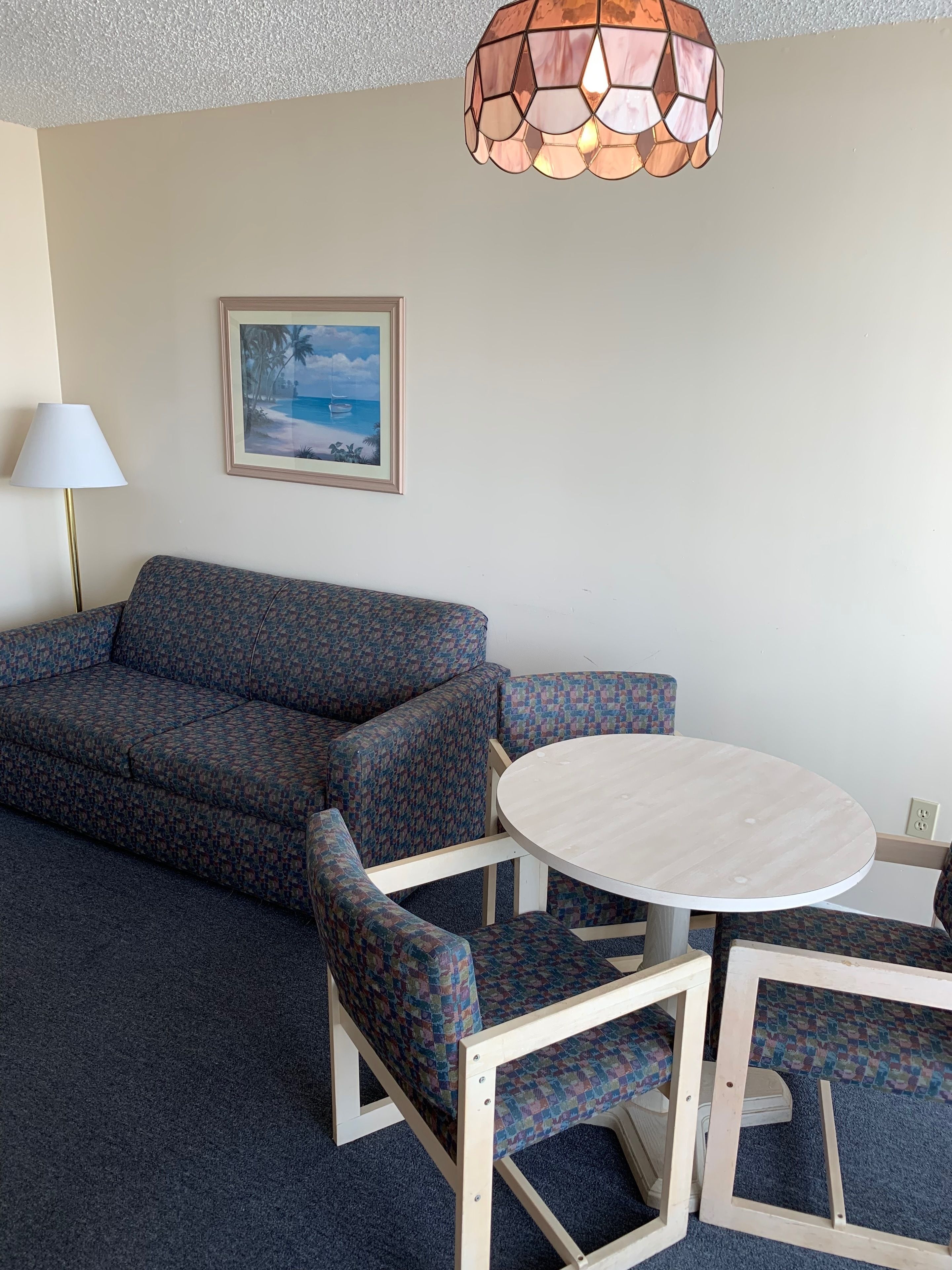 A room with a patterned sofa, a round table, and a hanging light fixture.