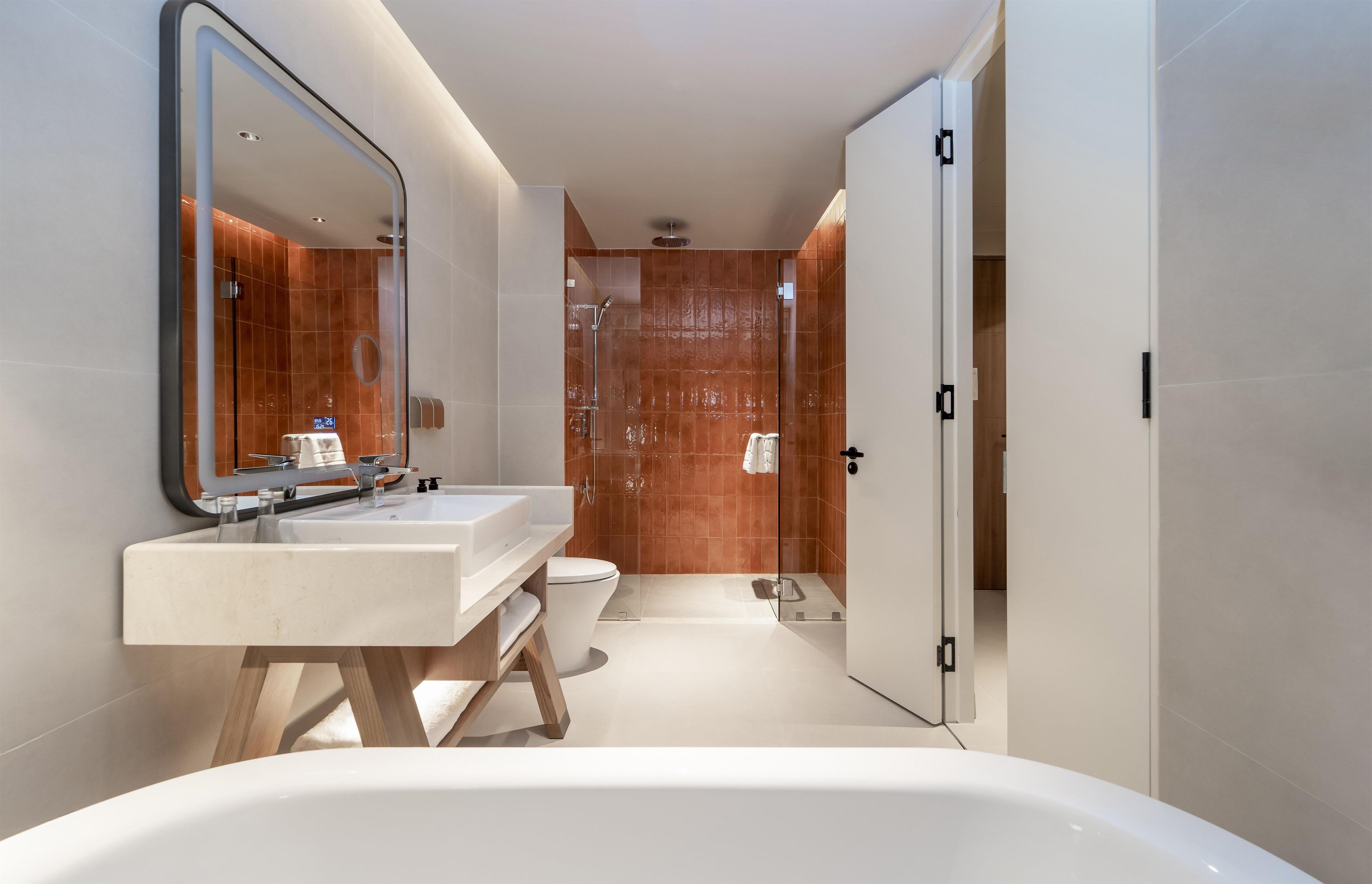A modern bathroom with a freestanding bathtub, a large mirror, and a separate toilet area.