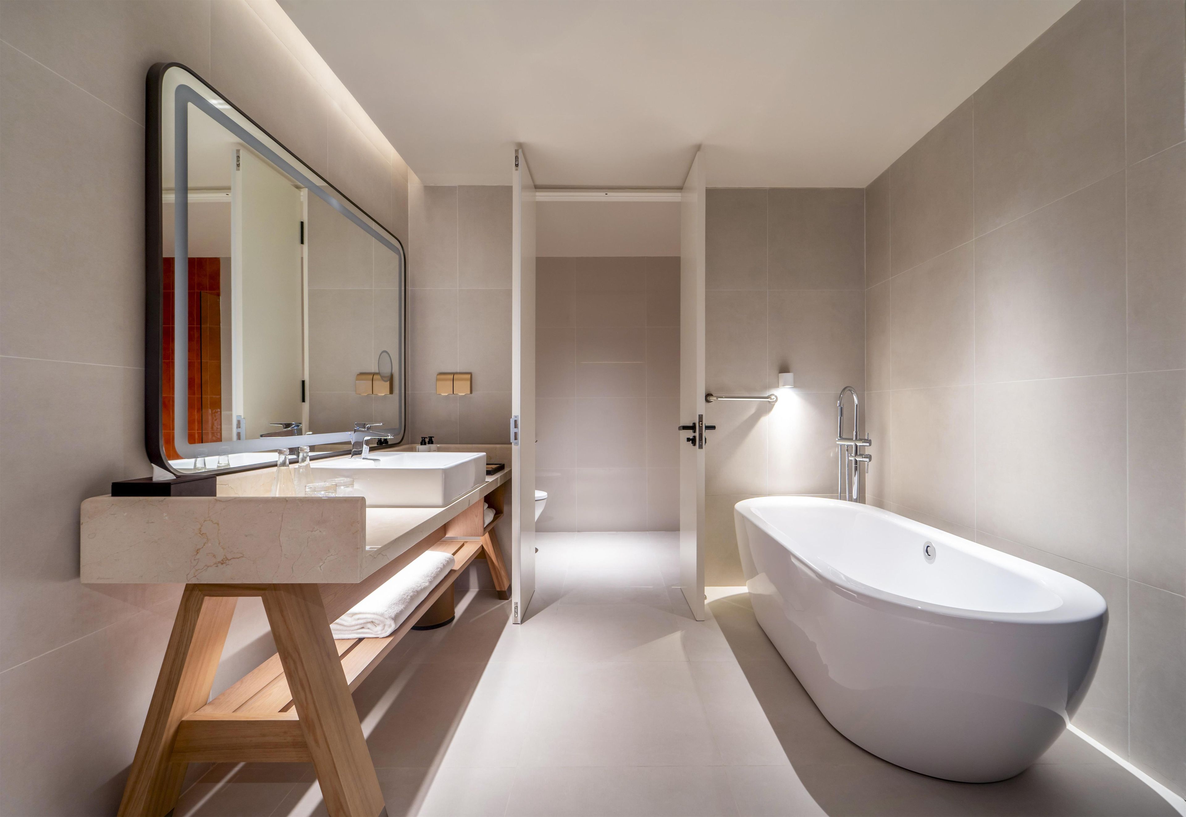 Un baño moderno con una bañera independiente, un espejo grande y un tocador con encimera de mármol.