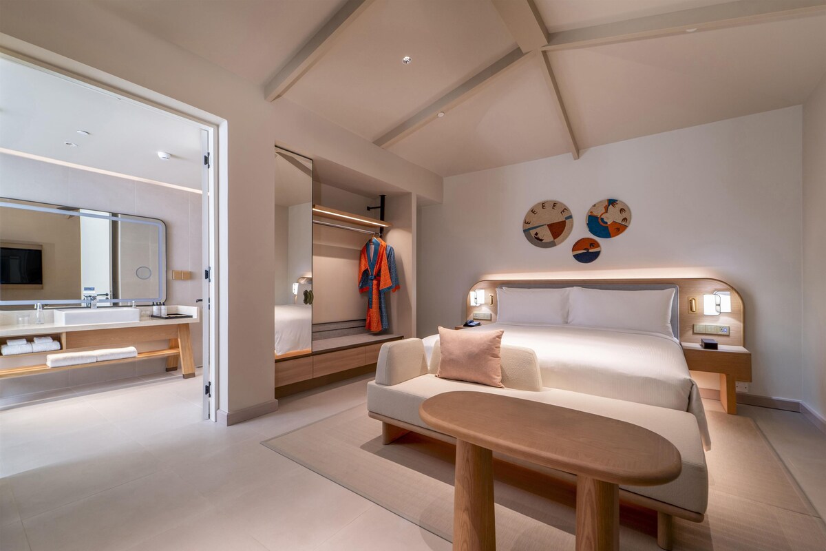 A modern hotel room with a bed, bedside tables, a bench, a mirror, and a wall with decorative plates.