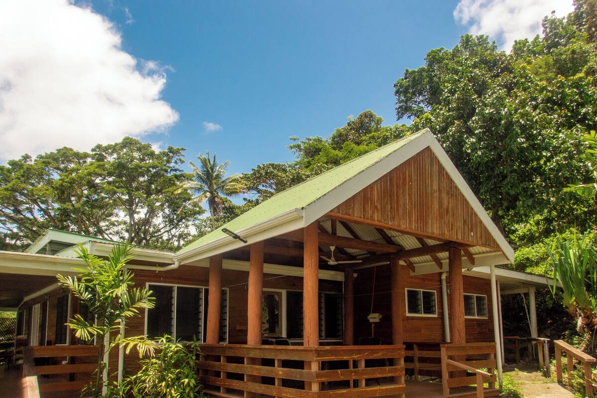 A wooden cabin with a porch, surrounded by lush greenery and trees.