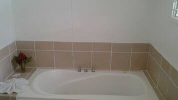 A standard rectangular bathtub with a white interior, beige tiled walls, and a small vase with a red flower on the left side.