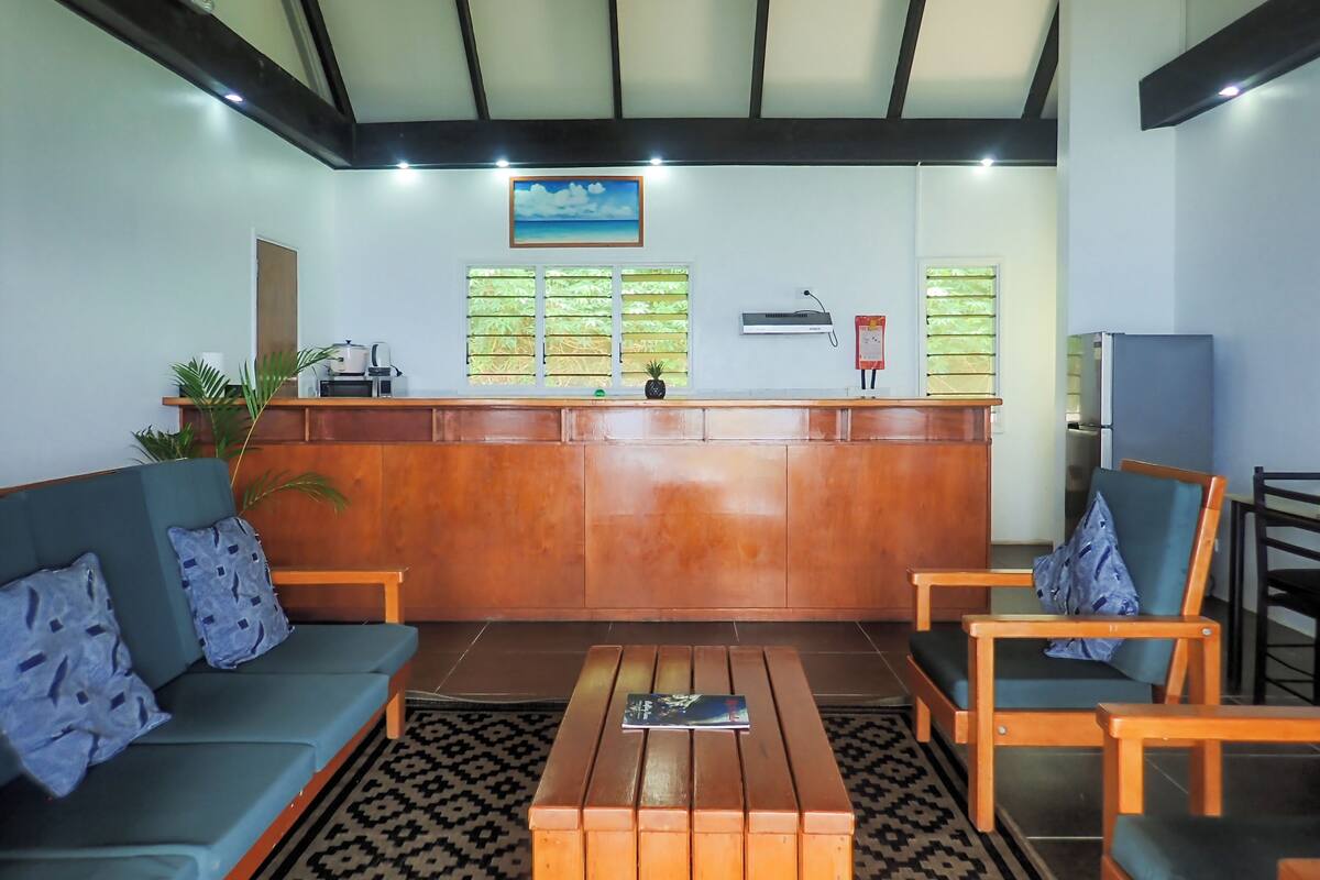 A reception area with a wooden reception desk, a blue sofa, two wooden chairs, a patterned rug, and a framed picture on the wall.