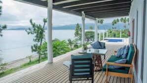 A wooden deck with a view of the sea and mountains, a table with chairs, and a sofa with cushions. - Daku Resort (Savusavu)